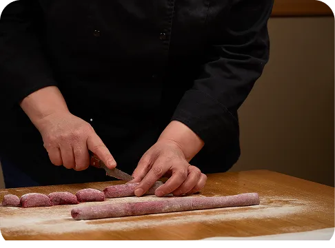 Une cuisinière découpe des pâtes fraîches sur un plan de travail fariné.